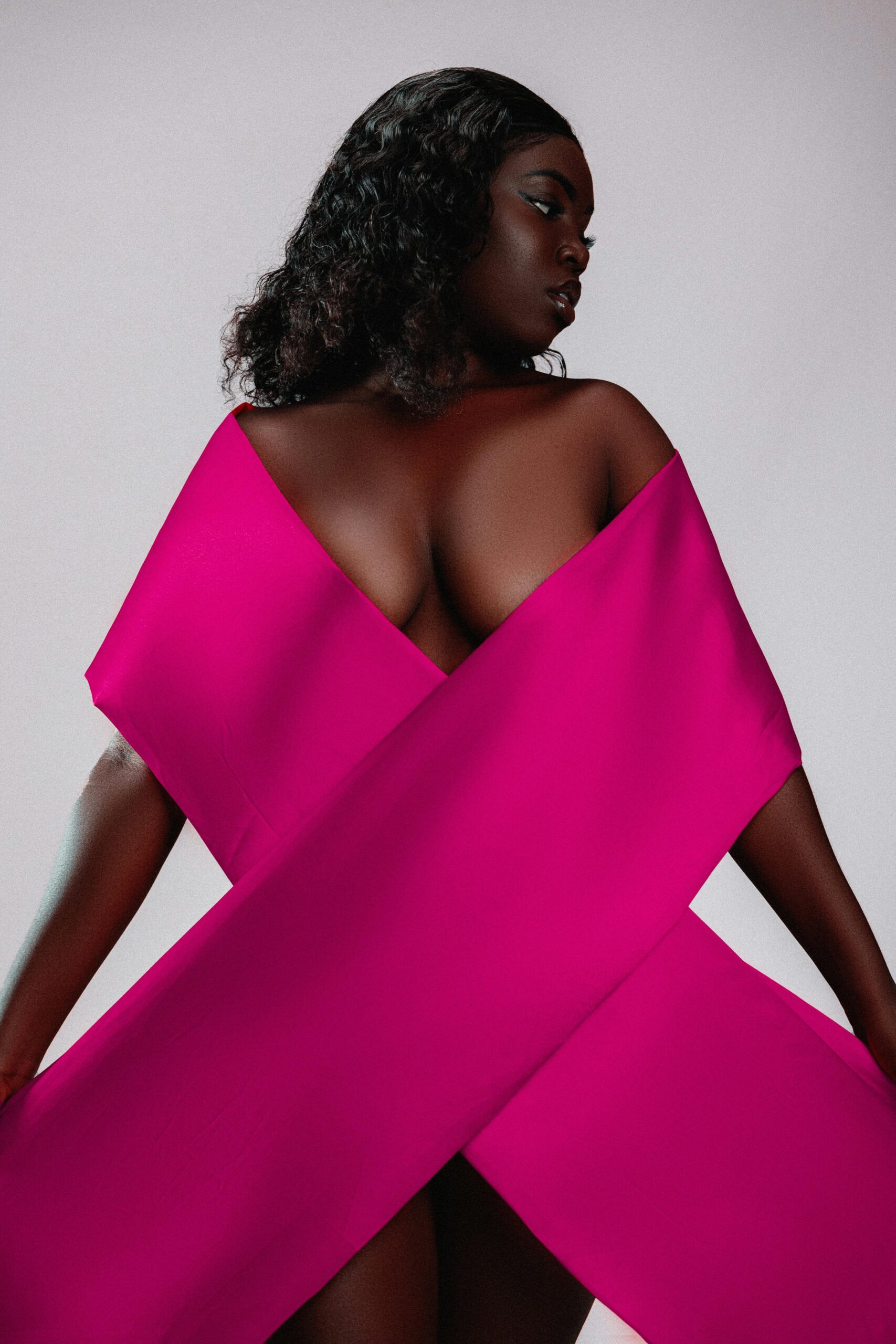 Striking studio portrait of a woman posing with a pink ribbon, symbolizing breast cancer awareness.